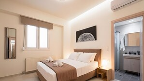 A modern bedroom with a large bed, a bedside table, a nightstand, a window with blinds, a wall-mounted picture, and an adjoining bathroom. - Apartment 'Zoelgrek Luxury Suite 1' with Private Terrace, Wi-Fi and Air Conditioning (Iraklio)