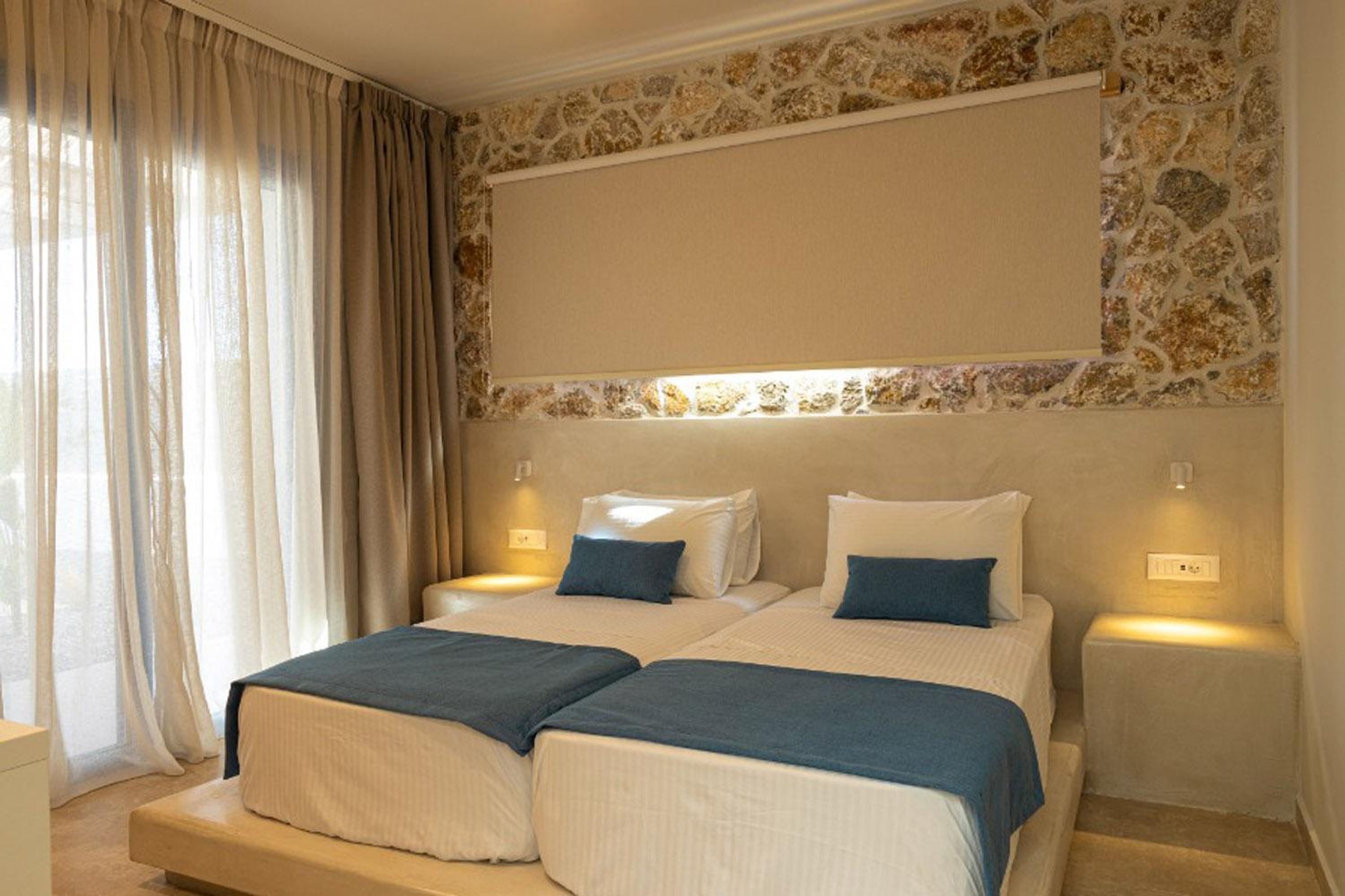 A double room with two beds, a stone wall, and a window with curtains.
