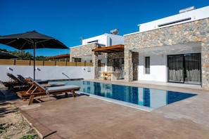 Ein moderner Poolbereich mit Liegestühlen, einem Tisch und einem Gebäude mit Naturstein-Fassade.