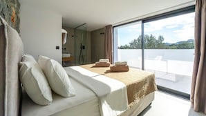 Ein modernes Hotelzimmer mit einem großen Bett, einem Balkon mit Blick und einem Badezimmer mit Spiegel und Handtuchhalter.