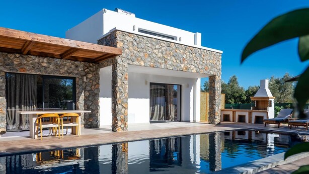 Ein modernes Haus mit Natursteinfassade, einem Schwimmbecken und einer Terrasse mit Gartenmöbeln.