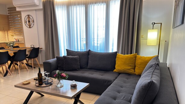 A modern living room with a sectional sofa, a coffee table, and a dining area with chairs and a table. - Zoelgrek Luxury Suite 2 Apartment with Shared Terrace, Wi-Fi & Air Conditioning (Iraklio)