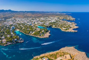 An aerial view of a coastal town with buildings along the shoreline, boats in the water, and a clear sky. - Villa del la Vilar in Mallorca (Pollença)