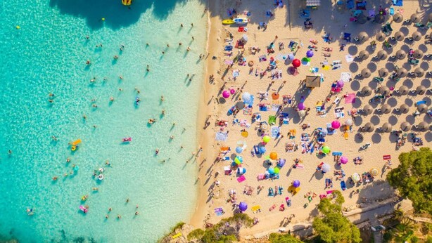 An aerial view of a beach with clear turquoise water, numerous umbrellas, and beach chairs. - Villa del la Vilar in Mallorca (Pollença)