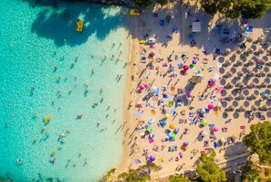 Egy tengerpart légi felvételén látható a kristálytiszta, türkizkék víz, a számos napernyő és a strandfelnapozók.