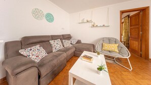 A living room with a brown sofa, a white coffee table, a grey chair, and decorative wall art. - Villa del la Vilar in Mallorca (Pollença)