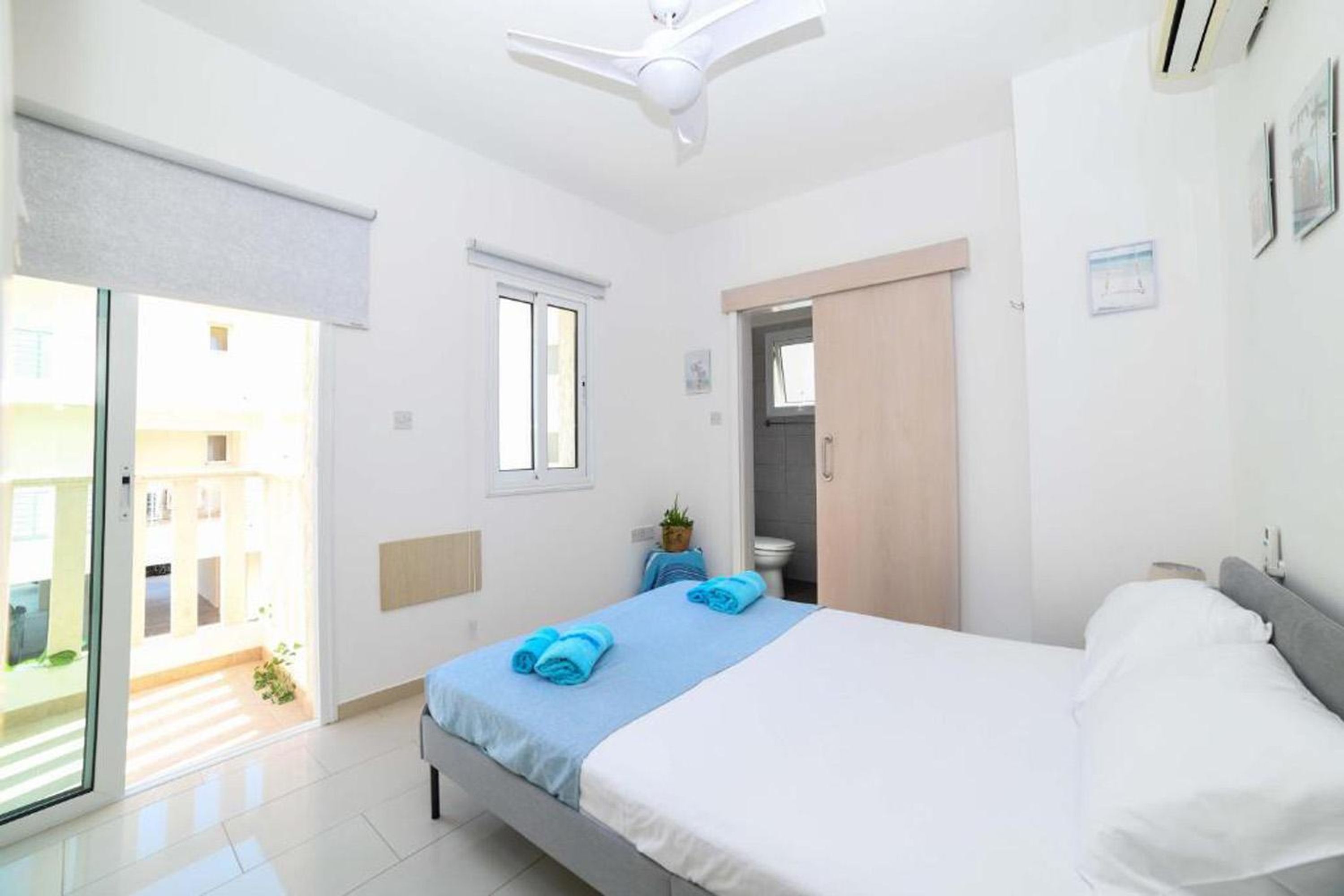 A bedroom with a bed, a ceiling fan, a window, and a door leading to a bathroom.