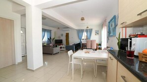A modern living room with a dining area, a kitchen, and a visible door leading to another room. - Villa Chromata in Pernera (Paralimni)
