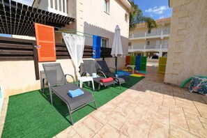 Um pátio com área de estar externa, piscina e um edifício com varandas.