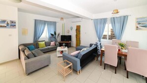 A modern living room with a sofa, a TV, a dining table with chairs, and a staircase. - Villa Chromata in Pernera (Paralimni)