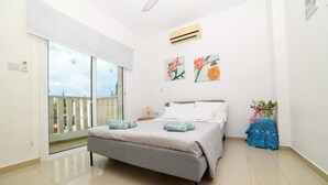 A bedroom with a bed, a sliding glass door to a balcony, and two wall-mounted air conditioning units. - Villa Chromata in Pernera (Paralimni)