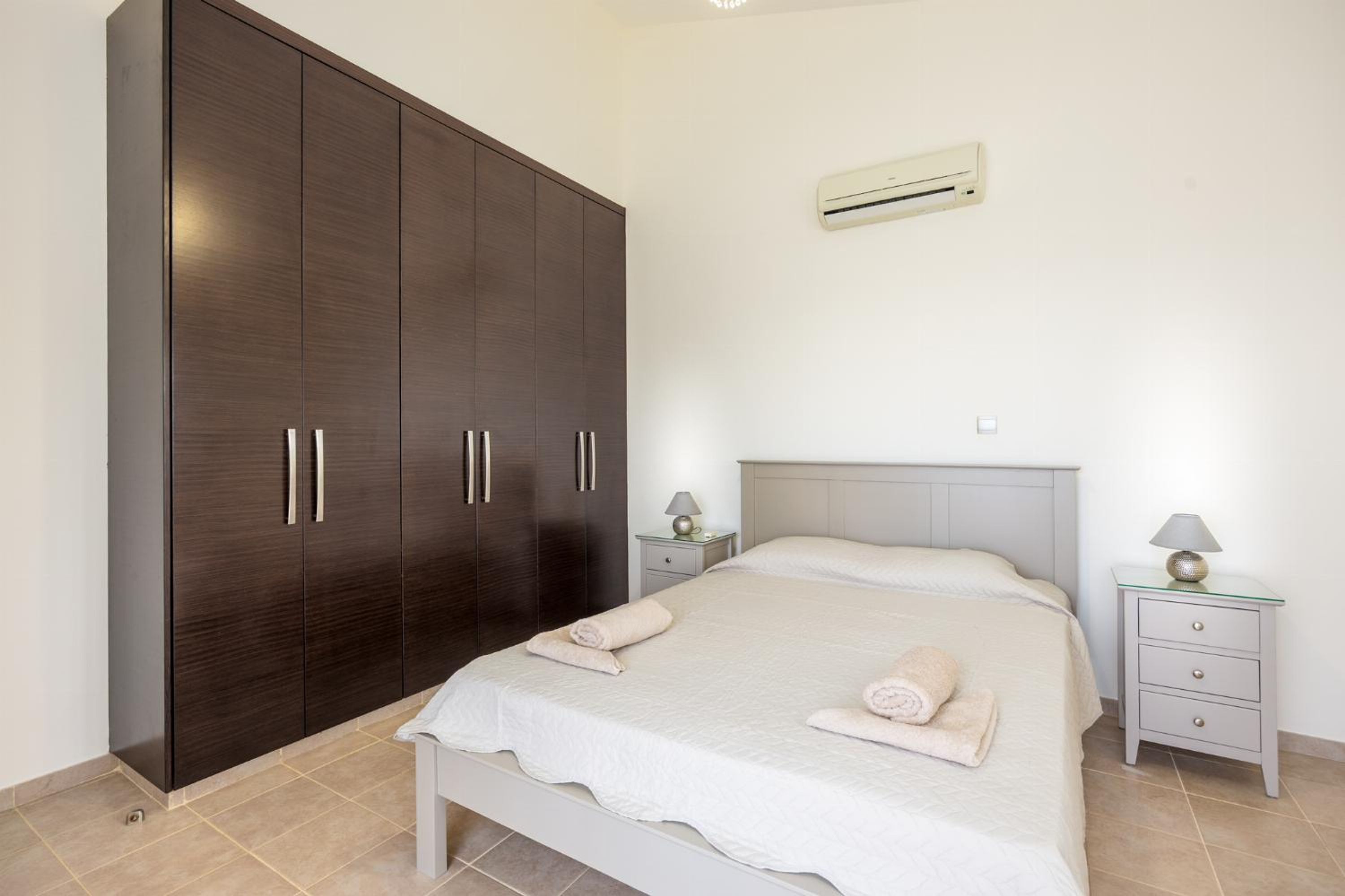 A bedroom with a bed, nightstands, a wardrobe, and an air conditioning unit.
