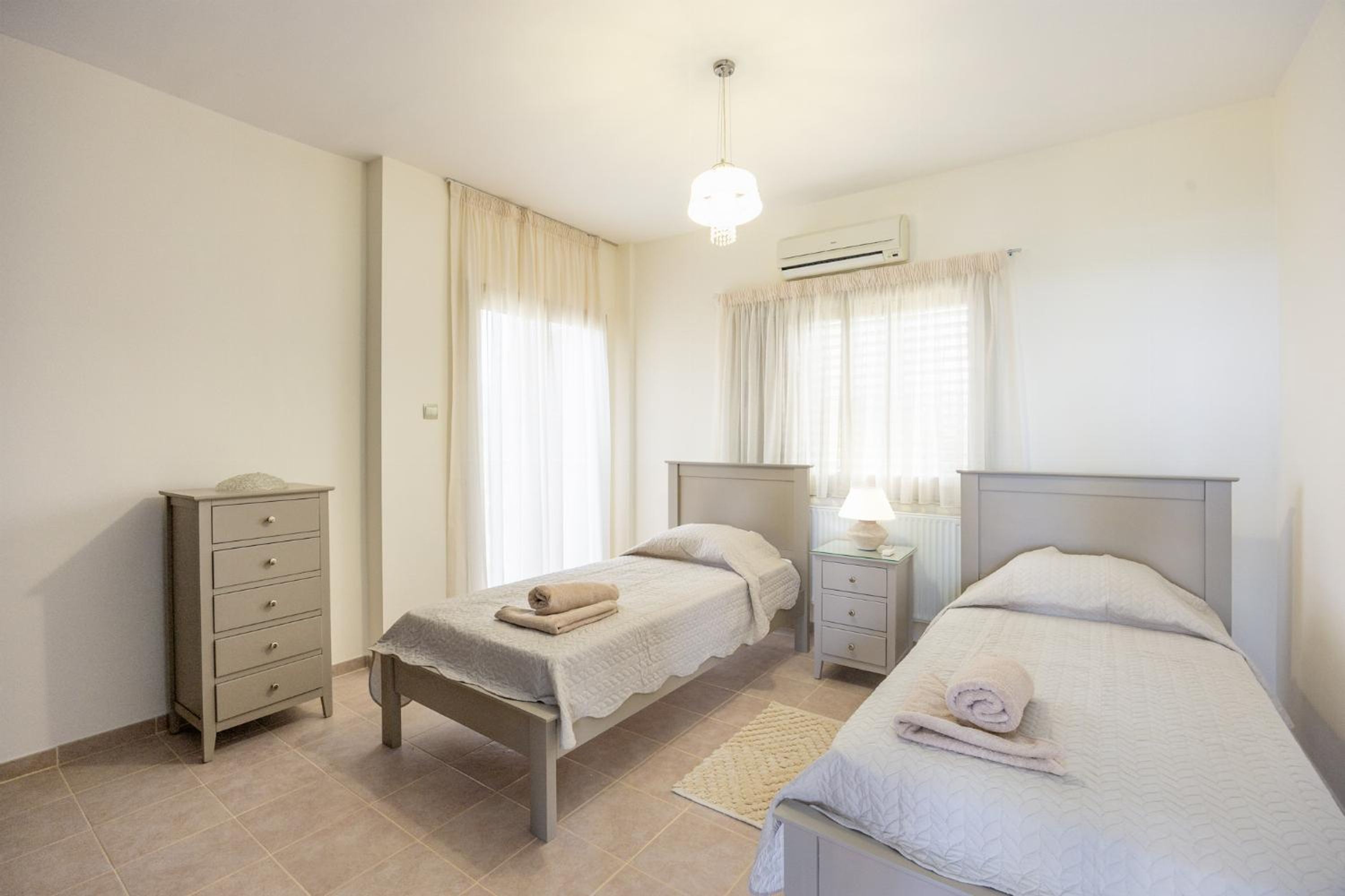 A bedroom with two beds, a dresser, a nightstand, and an air conditioning unit.