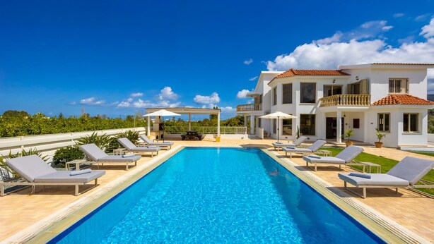 A swimming pool with lounge chairs, a covered seating area, and a two-story building with a balcony.