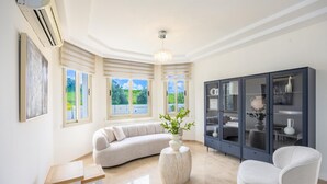 A modern living room with a curved sofa, a round table, a cabinet with glass doors, and a ceiling fan.