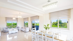 A spacious living area with a dining table, white furniture, and large windows with a view.