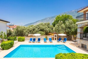 A pool with blue chairs, a stone wall, and a mountain in the background. - Golden Trio Villa in Oludeniz (Fethiye)