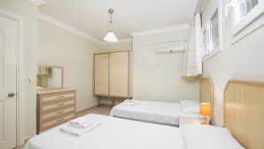 Ein Hotelzimmer mit zwei Betten, einem Schminktisch, einem Spiegel, einer Klimaanlage und einem Fenster mit Vorhängen.