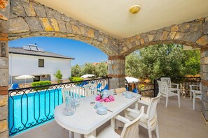 A covered outdoor dining area with stone arches, a pool, and white furniture. - Golden Trio Villa in Oludeniz (Fethiye)