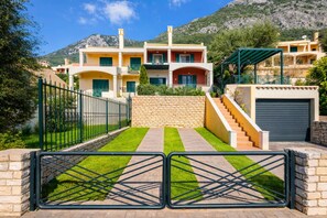A multi-story building with a stone wall, a gated entrance, and a staircase leading to the upper levels. - Golden Tiara Apartment (Corfu)
