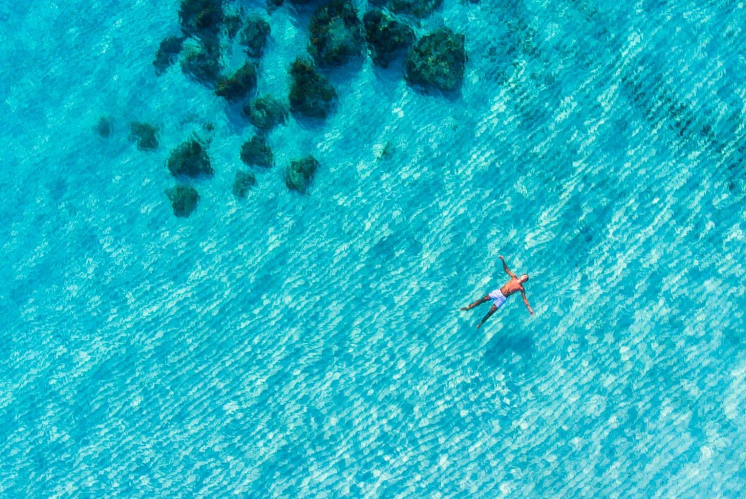 Una persona nadando en agua azul cristalina con rocas visibles bajo el agua.