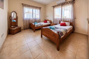 A room with two wooden beds, a wooden dresser, a mirror, and a window with sheer curtains. - Argiro Bright Villa in Pernera (Paralimni)