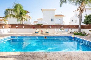 A swimming pool with a wooden deck, lounge chairs, and a palm tree. - Argiro Bright Villa in Pernera (Paralimni)