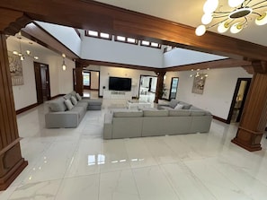 A spacious living room with a large sectional sofa, a flat-screen TV, and a high ceiling with skylights. - Villa Ballena Azul in Teguise (Teguise)