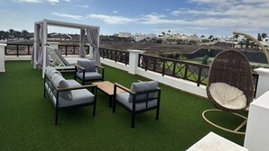 Een terras op het dak met kunstgras, tuinmeubilair en uitzicht op een kustlandschap.