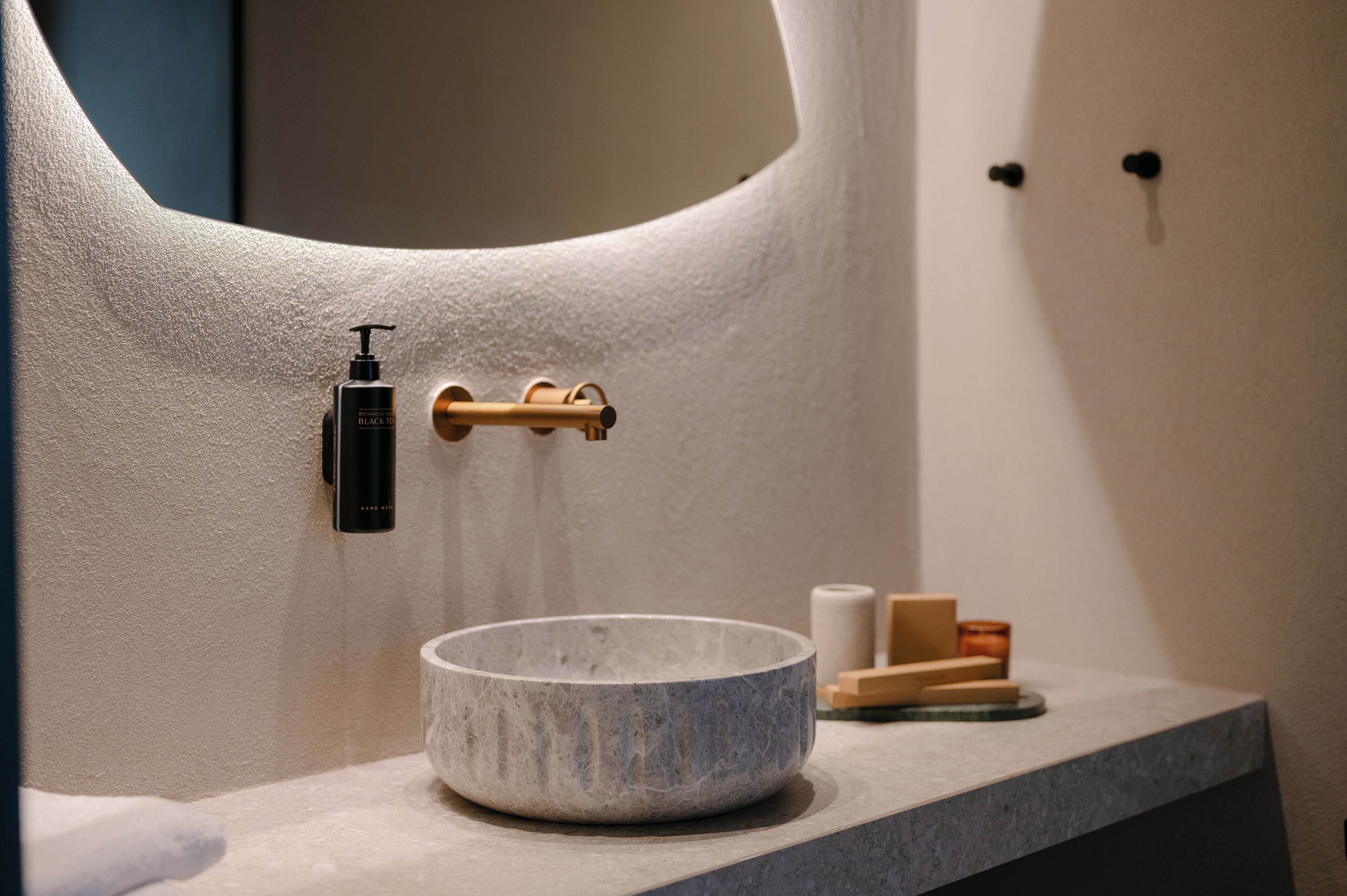 A bathroom with a stone basin, a black bottle, and wooden items on the counter.