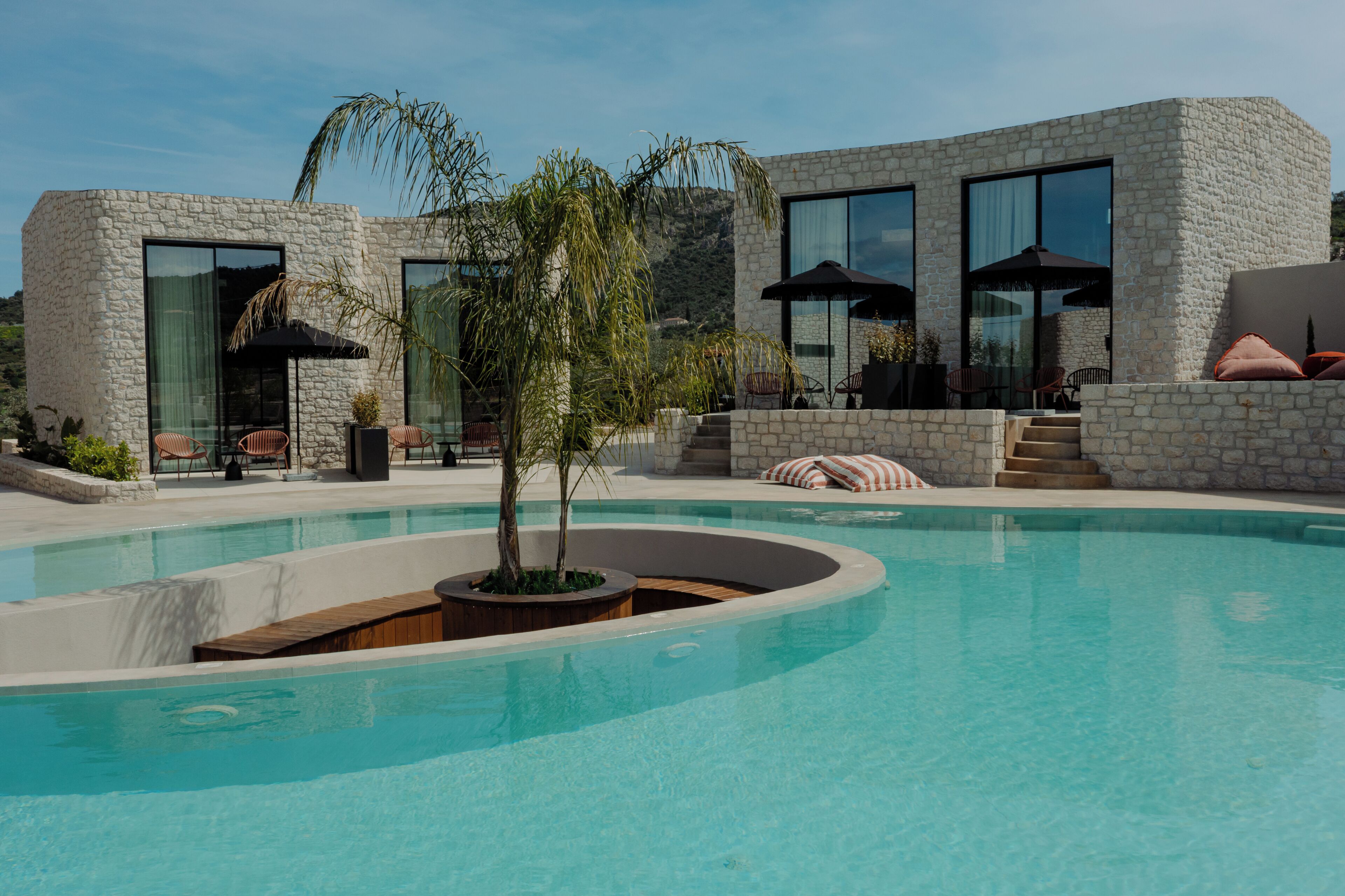 Un área de piscina moderna con paredes de piedra, amplias ventanas y mobiliario exterior.