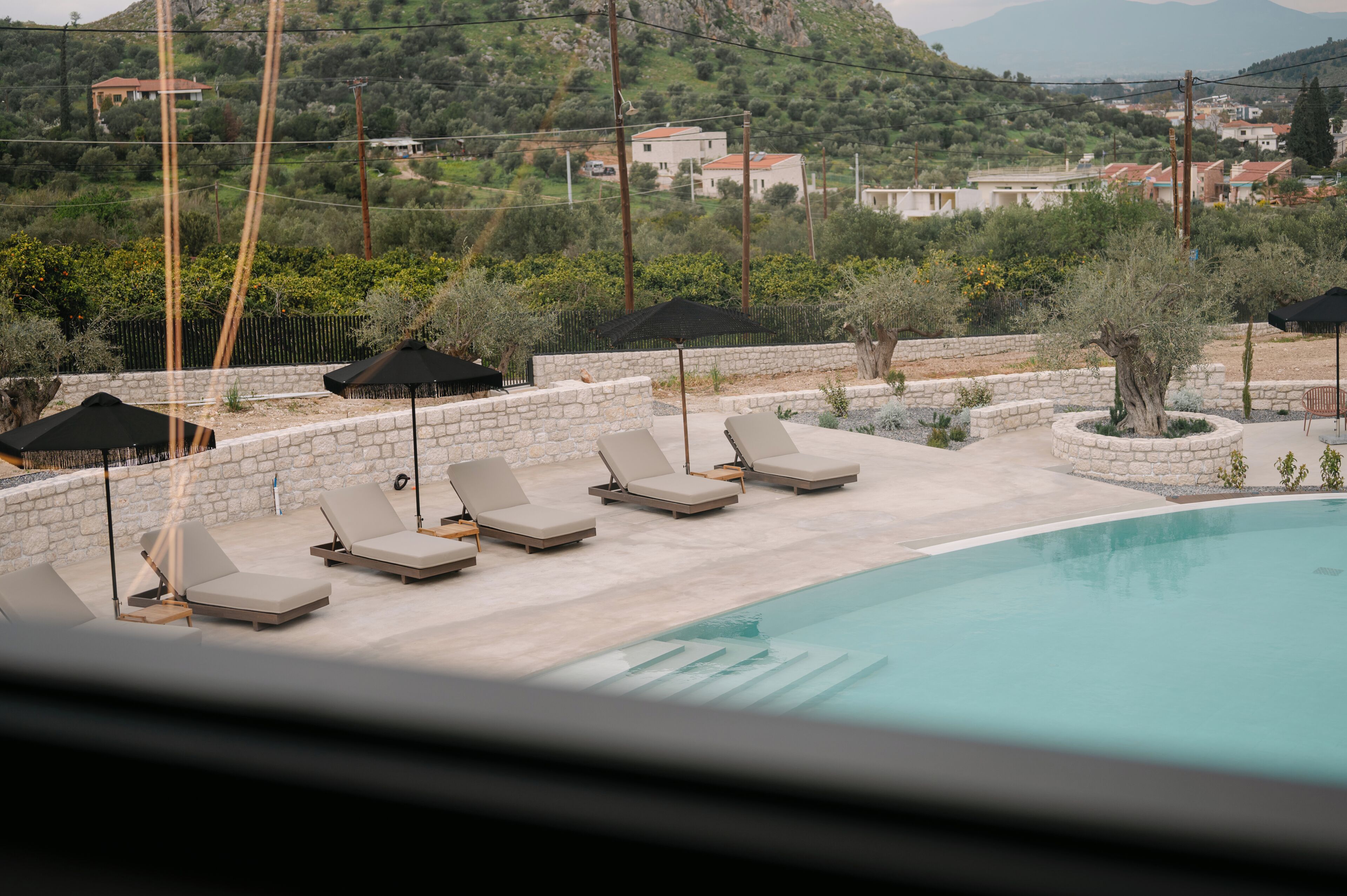 A poolside area with lounge chairs and umbrellas, surrounded by stone walls and greenery.