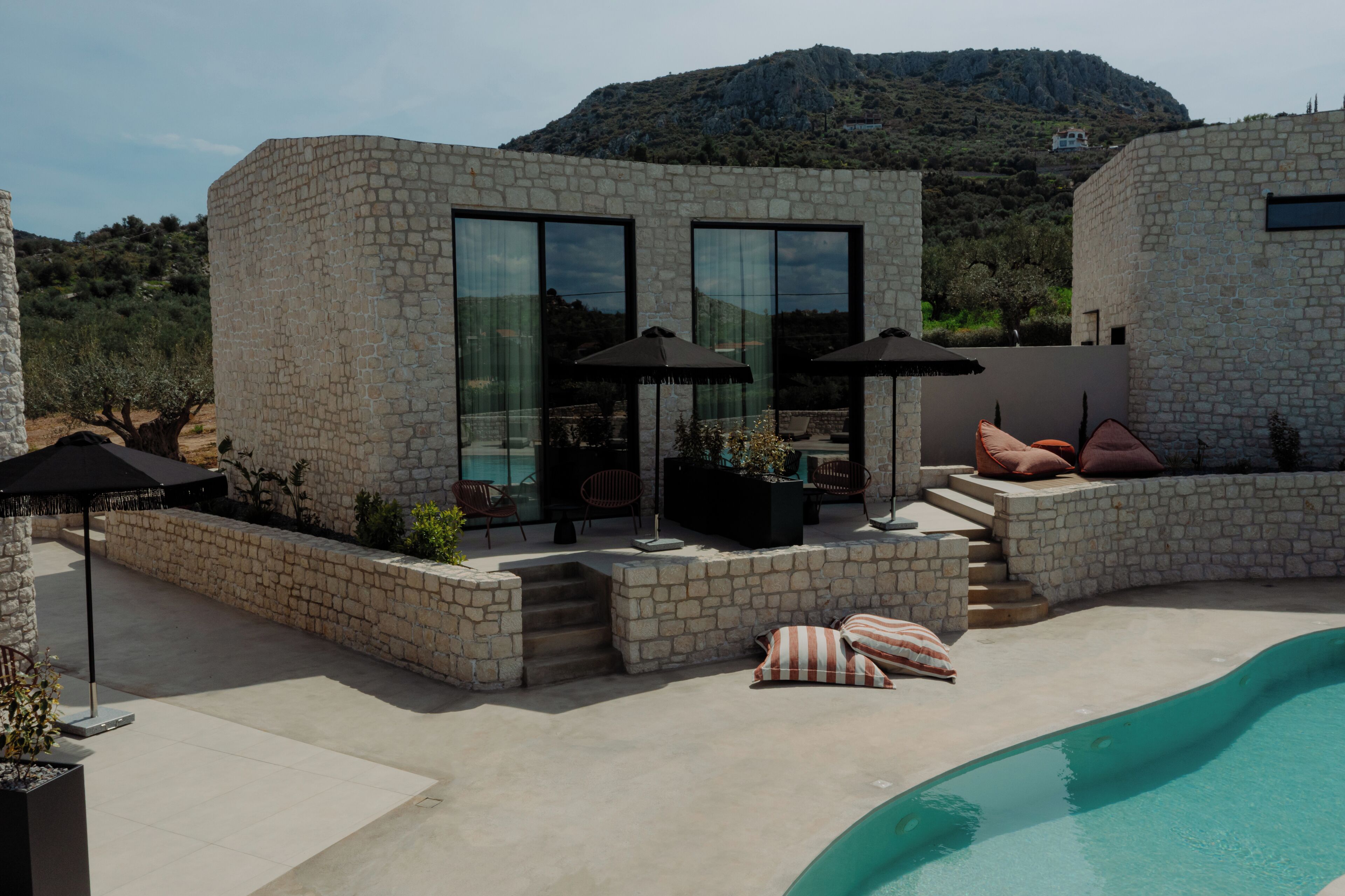 A modern stone building with large windows, outdoor seating, and a pool.