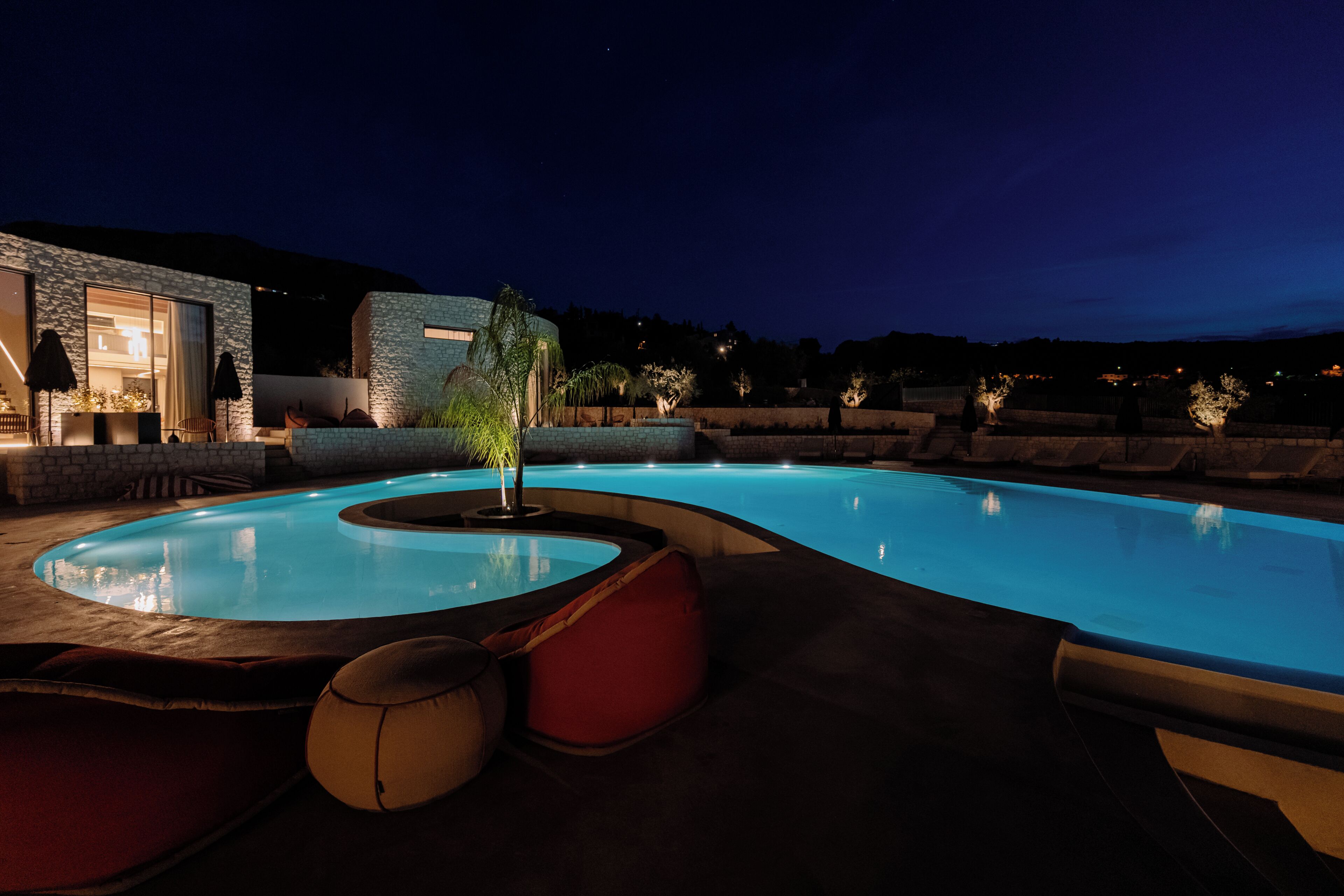 A swimming pool with a curved design, surrounded by stone walls and outdoor seating.