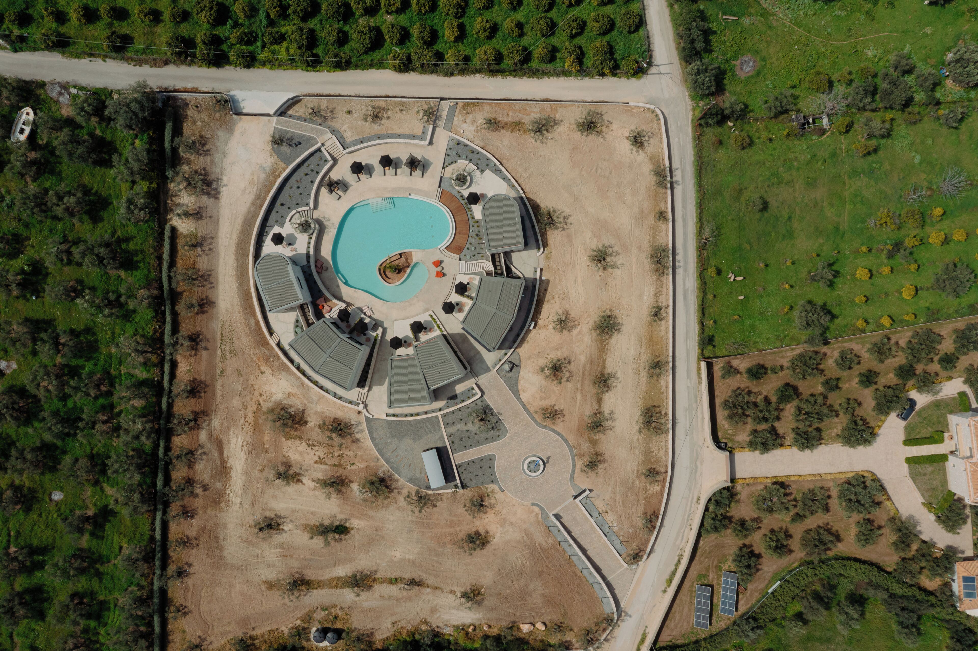 An aerial view of a resort with a central swimming pool, multiple lounge areas, and a parking lot.