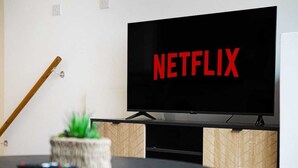 En tv med Netflix-logotypen på ett stativ, en fjärrkontroll och en liten växt på ett bord.