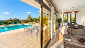 A pool with a view of the ocean, a dining area, and a living room with a sofa and a coffee table.