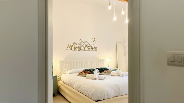 Ein Schlafzimmer mit Bett, Nachttisch, Wandleuchte und Wandbild.
