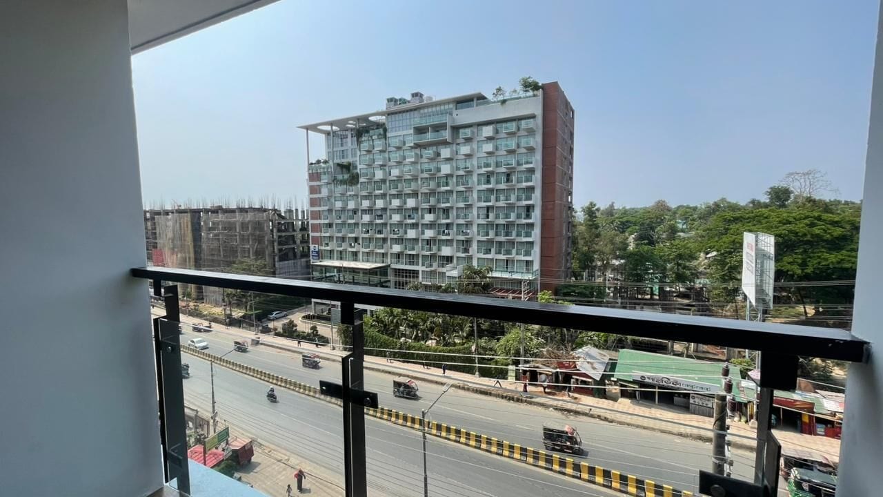 A high-rise building with multiple balconies, a busy street with vehicles, and a clear sky.