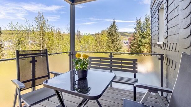 A balcony with a table and chairs, a potted plant, and a view of trees and buildings. - Apartment 'Burgquartier' with Balcony and Wi-Fi (Schmallenberg)