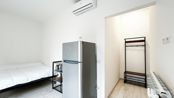 A small, modern room with a bed, a built-in refrigerator, a wardrobe, and a radiator. - Monfalcone Milano (Milan)