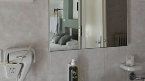 Un bany amb un mirall gran, un lavabo, un assecador de cabells, una ampolla d'oli d'oliva i un escurapulles.