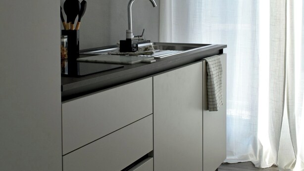 Una cuina moderna amb un rentatge d'acer inoxidable, un taulell negre i una finestra amb cortines de tela fina.