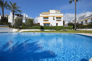 Une piscine à l’eau d’un bleu limpide, entourée d’un bâtiment blanc agrémenté de touches de jaune et doté de nombreux balcons.