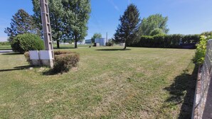 Un espacio al aire libre con césped, árboles, una estructura de concreto y un edificio al fondo.