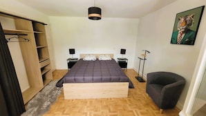 Un dormitorio con cama, mesitas de noche, un armario, una silla y un cuadro en la pared.