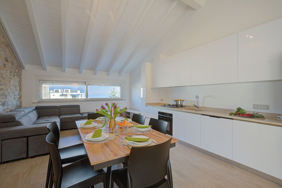A modern kitchen with white cabinets, a dining table set for four, and a built-in oven.