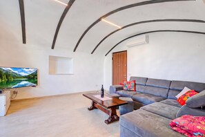 Ein modernes Wohnzimmer mit Flachbildfernseher, Couchtisch aus Holz, grauem Sofa und farbenfrohem Zierkissen.