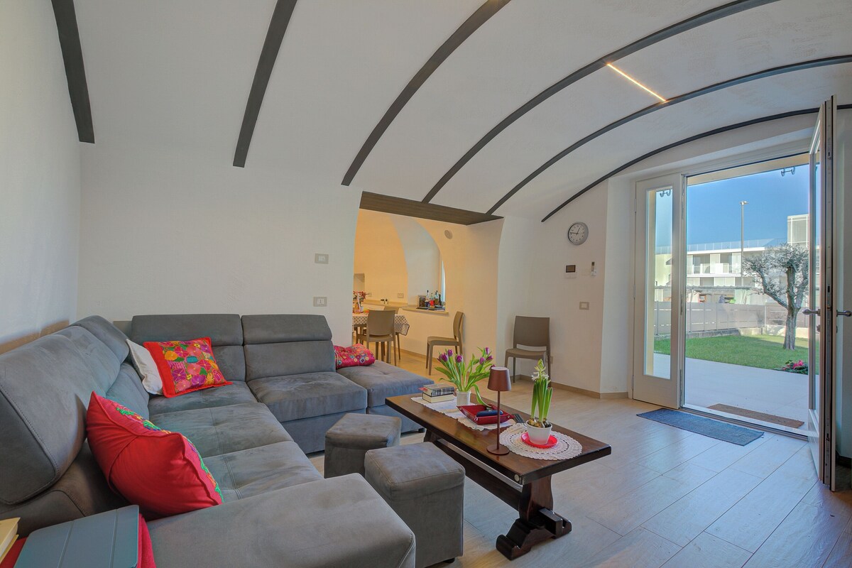 A modern living room with a grey sofa, a coffee table, and a dining area in the background.