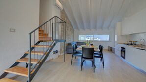 A modern kitchen with a built-in oven, a dining area with a table and chairs, and a staircase with a railing.
